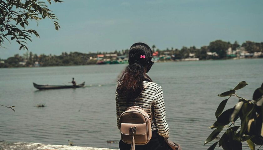 A woman with a backpack sits by the river in Kochi, India, enjoying a peaceful summer day.